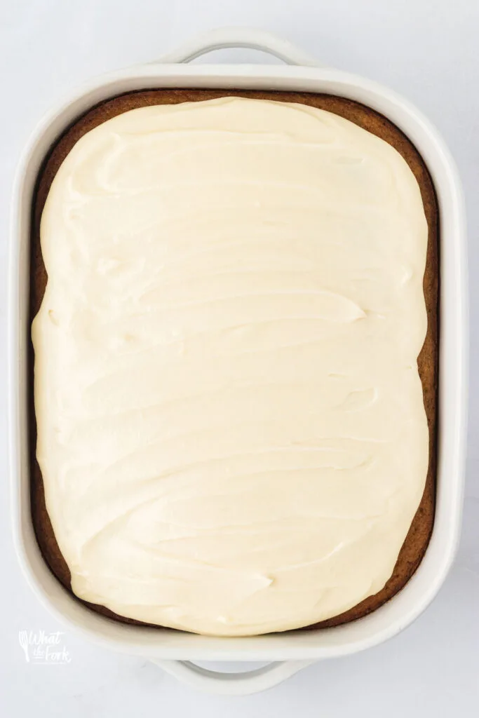 gluten free banana cake baked topped with cream cheese frosting in a white 9x13 baking pan