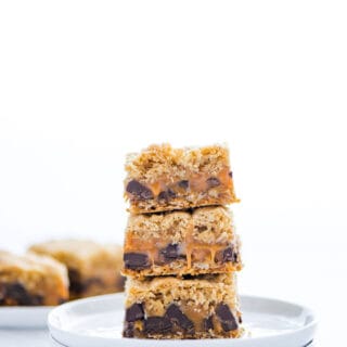 3 gluten free carmelitas stacked on top of a stack of 2 small round white plates.