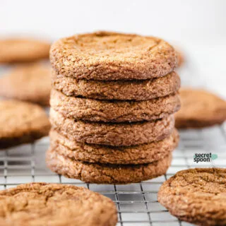 a stack of crispy Gluten Free Gingersnap Cookies on a metal wire rack with other cookies spread around