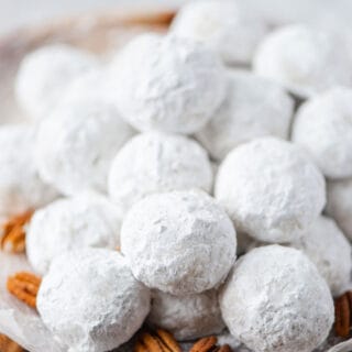 Traditional Gluten Free Mexican Wedding Cookies on a wax paper lined round wood platter with pecans for garnish
