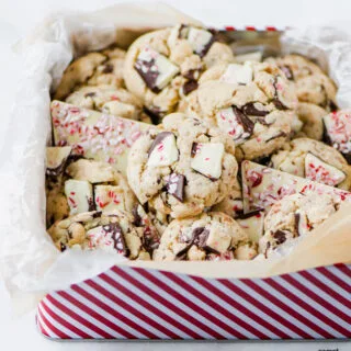 Gluten Free Chocolate Chip Peppermint Bark Cookies in a white and red striped cookie tin lined with white and natural parchment paper