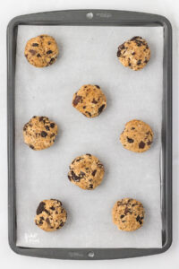 Gluten Free Oreo Chocolate Chip Cookie dough portioned out on a silver baking sheet lined with white parchment paper ready to be baked