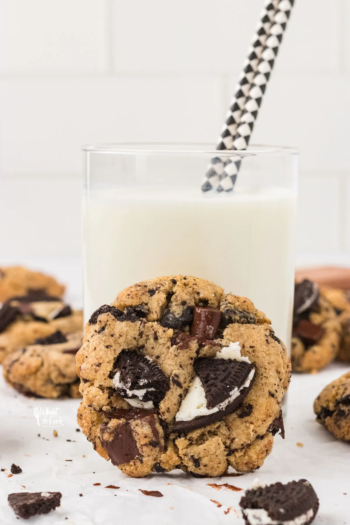 a Gluten Free Oreo Chocolate Chip Cookie leaning against a glass of milk with a black and white paper straw in it